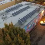 Musician’s Union 1 Aerial view showing solar panels on a flat roof beside a colorful mural-covered building and a parked white car along a street