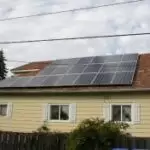 Residential Dwelling 3 1 Residential dwelling with a yellow exterior and solar panels installed on a sloped roof, suburban setting under a partly cloudy sky