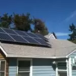 Residential Dwelling 4 1 Blue suburban house with solar panels mounted on a sloped roof, white trim, light gray roof, and clear blue sky in the background