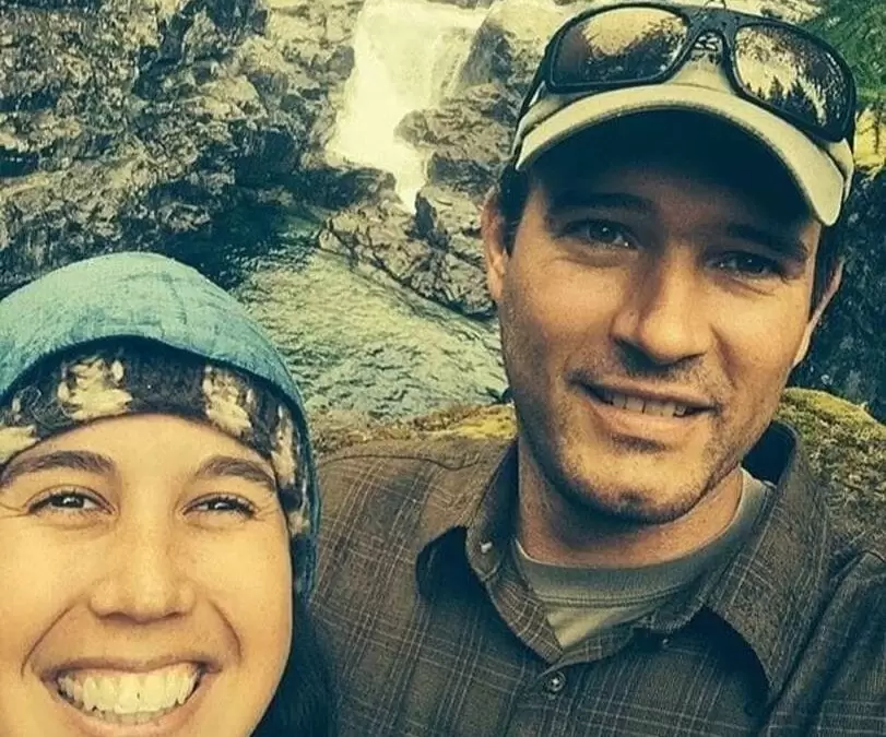 My Solar Story: Brion Wickstrom 4 Brion and Sarah posing together with a waterfall in the background, both wearing outdoor clothing and hats.