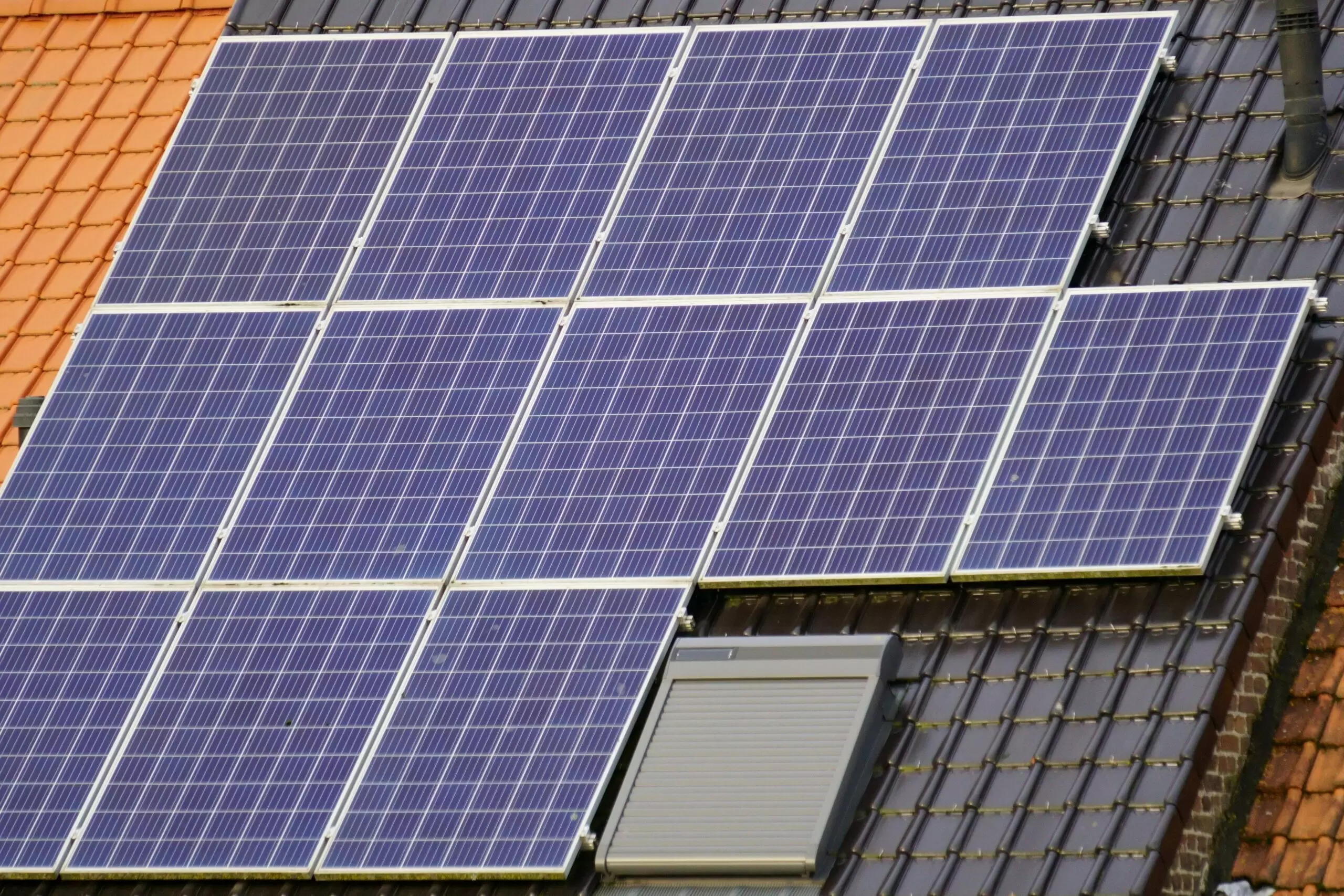 Solar panels arranged in a grid pattern on a sloped roof with a window below them.