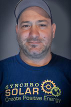 Man with a beard wearing a blue Synchro Solar t-shirt and a baseball cap.